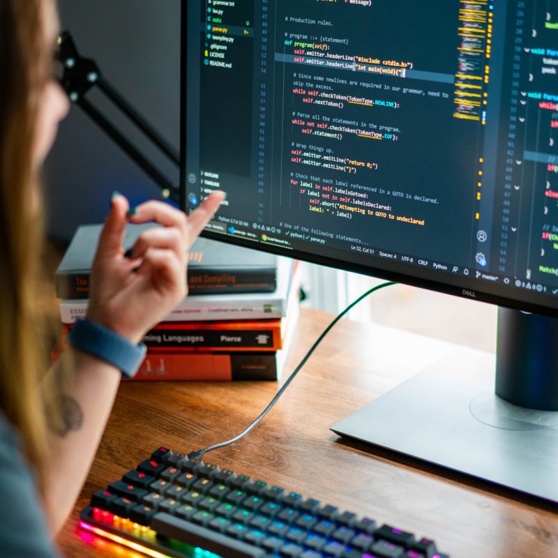 Picture of a woman working at a computer, pointing at the code on the monitor