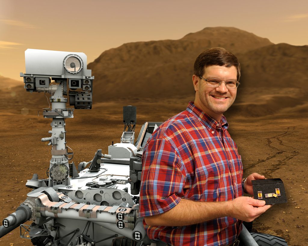 Ben Blalock posing with his chip technology with green screen Mars rover in the background